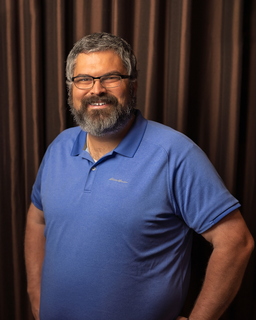 Man smiling, wearing glasses and blue polo shirt.