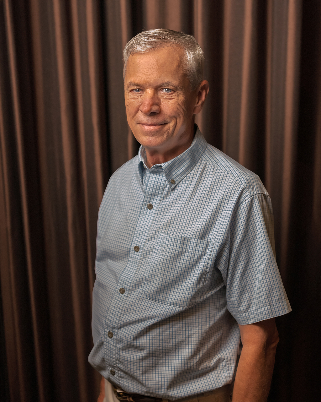 Smiling man in checkered shirt with curtains background.