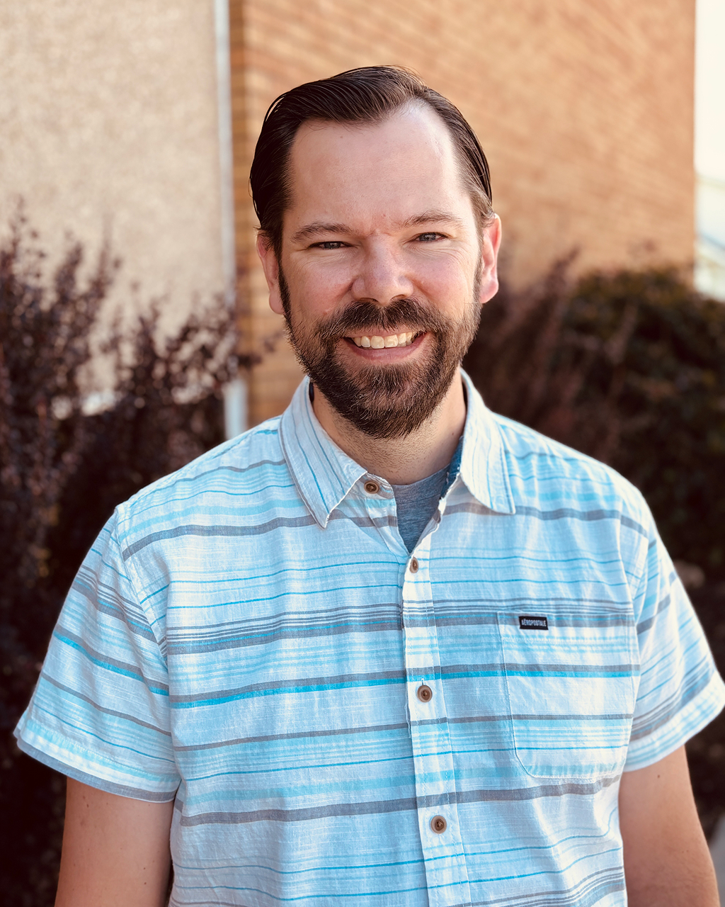 Smiling man in striped shirt outside building