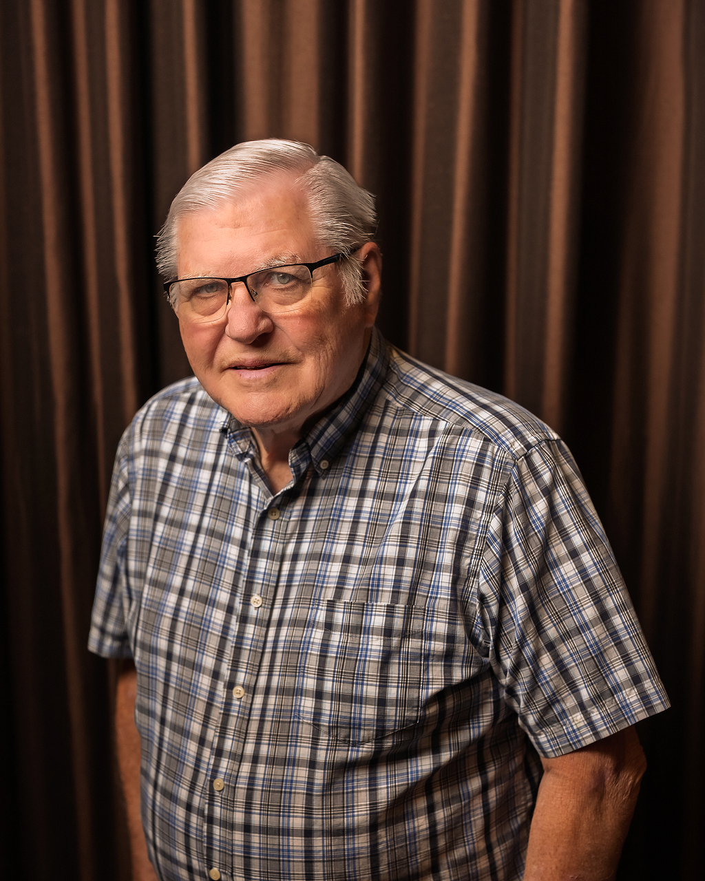 Elderly man in plaid shirt with glasses and curtains