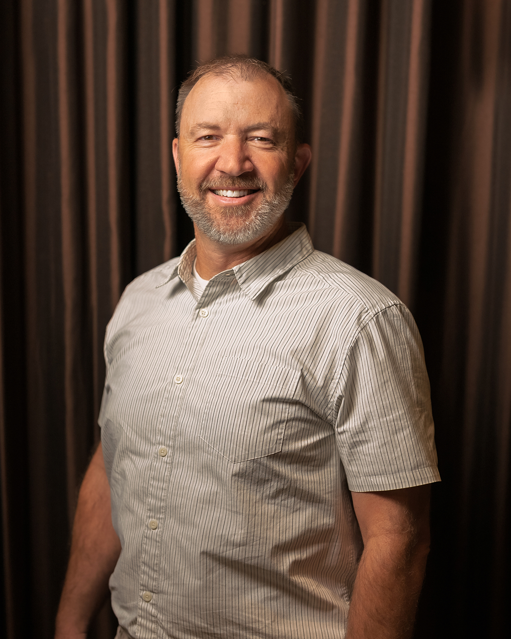 Person smiling with striped shirt in front of curtain.