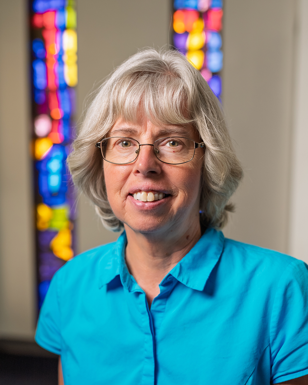Smiling woman in blue shirt, stained glass background.