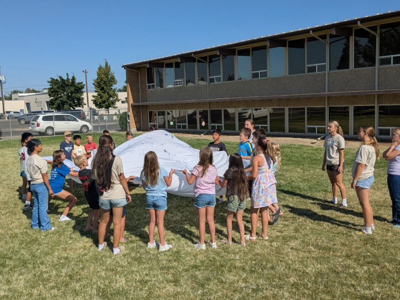 Kids playing parachute game on school lawn.