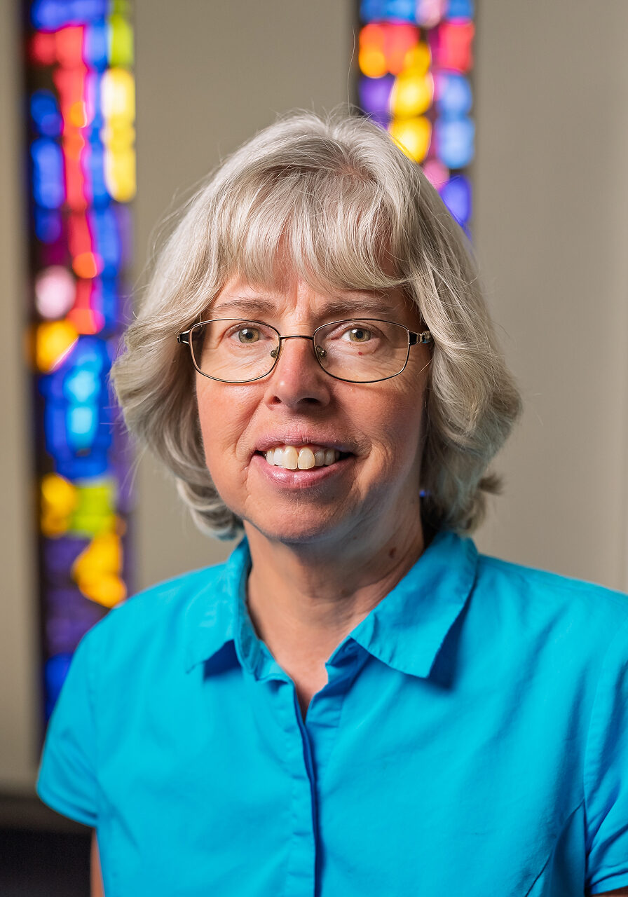 Smiling woman in blue shirt, stained glass background.